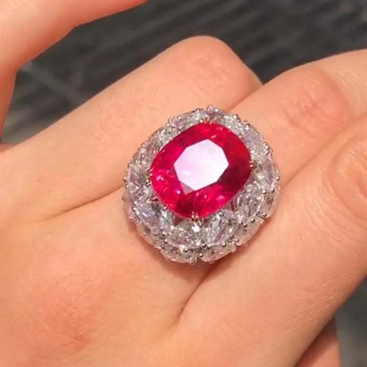 Close-up of a hand wearing The Crimson Star of Mogok 14.54ct neon red Jedi Spinel ring with a halo of clear gemstones.