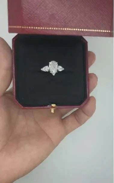 The Aurelia Sigil ring with a pear-shaped starforged diamond and two side stones in a gold setting inside a red jewelry box