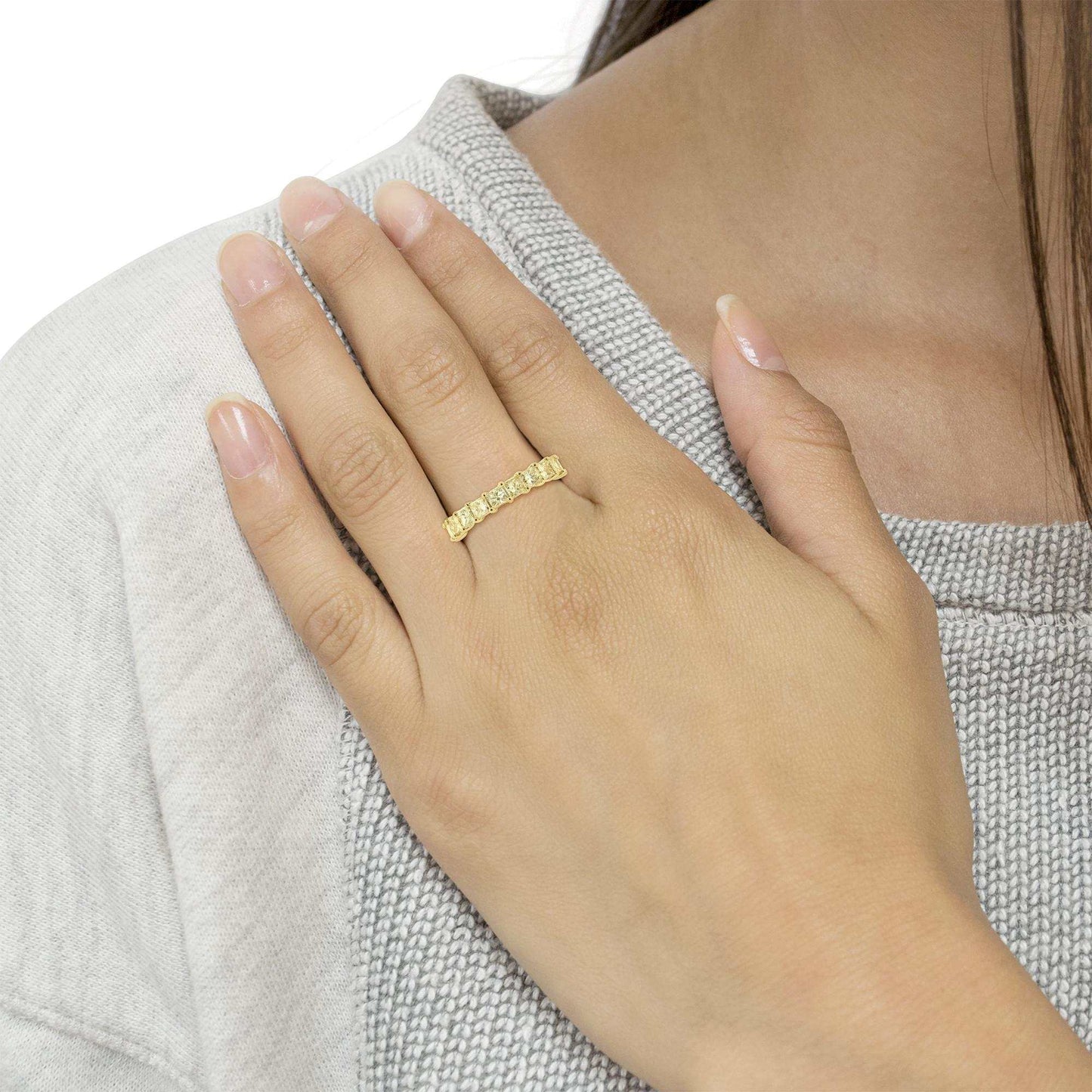 Hand wearing a 14K yellow gold eternity band ring set with princess cut diamonds in a shared prong setting.