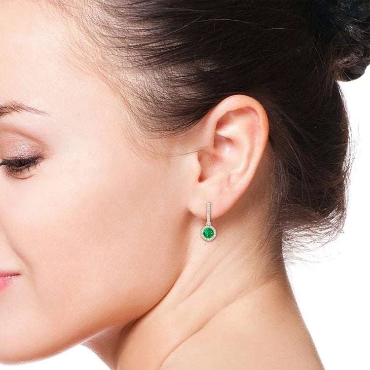 Woman wearing Emerald Radiance Halo Drop Earrings with vibrant green emerald and halo of sparkling stones