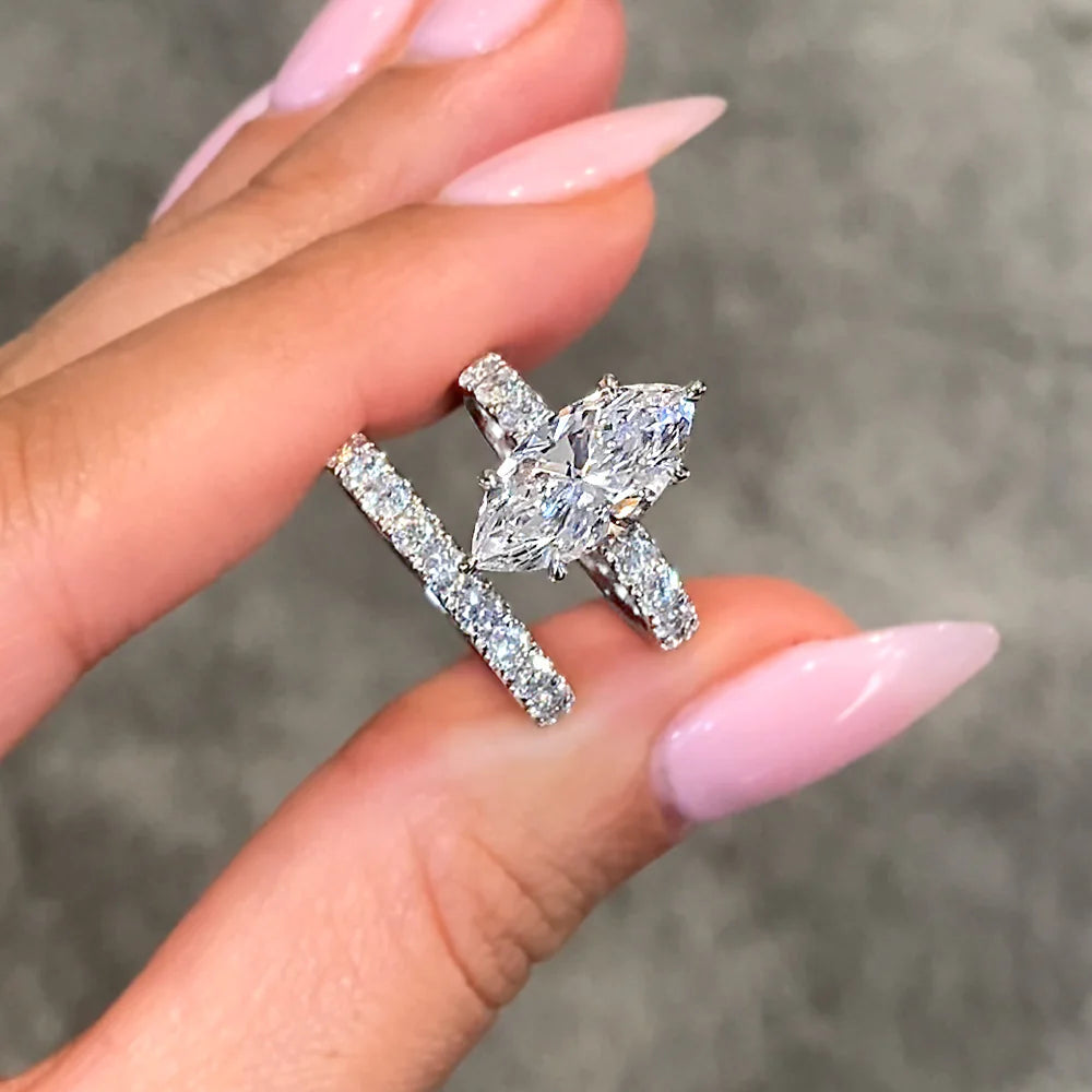 Close-up of Star-Forged Promise engagement ring and matching bridal band with marquise-cut diamond set in 14K white gold, held between manicured fingers