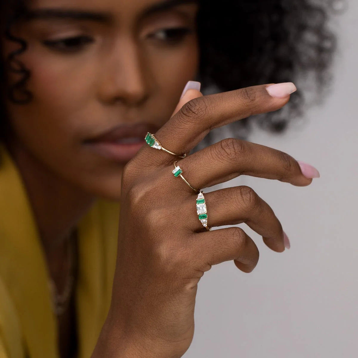 Close-up of a hand wearing the Hall of Emerald Ring in 14k yellow gold with natural rectangular emeralds and Asscher-cut diamond centerpiece