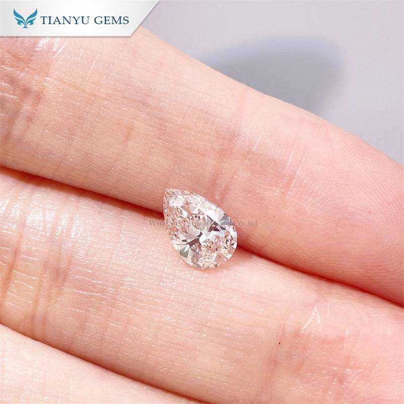Close-up of a cherry pink pear oval lab grown diamond on a fingertip, showcasing its clarity and shape.