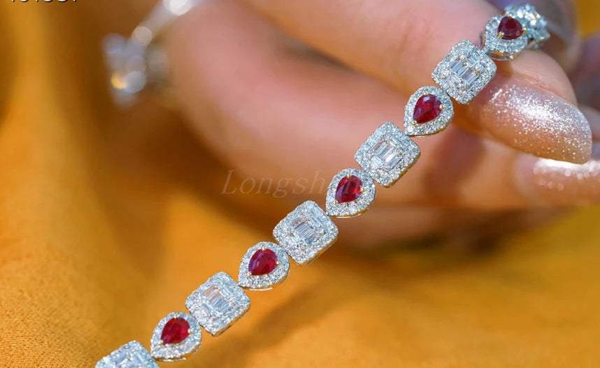 Pear shape ruby and baguette diamond square bracelet held by hand with glittery nails on a golden background