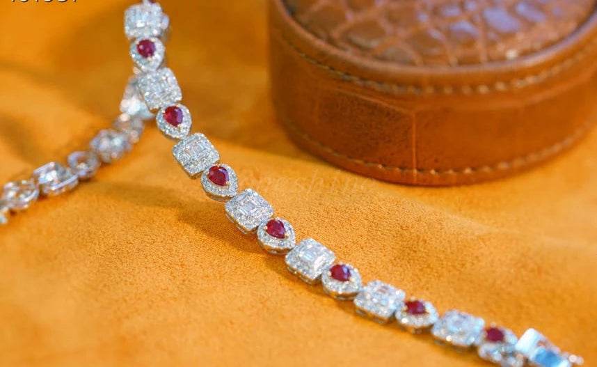 Pear shape ruby and baguette diamond square bracelet on a soft orange surface with a brown leather jewelry box in the background