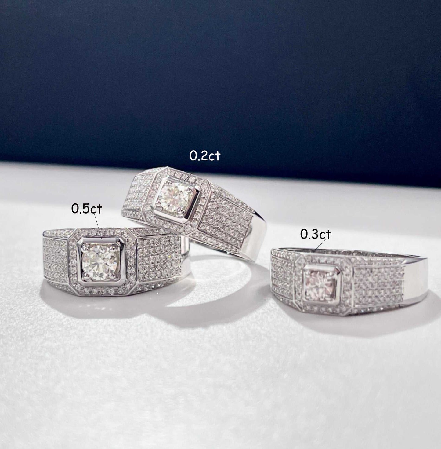 Three paved bling Wedding Men Rings with sparkling stones in varying sizes displayed on a white surface