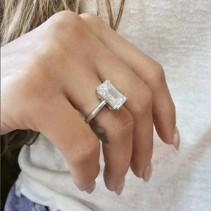 Close-up of a hand wearing the Eternity Prism 5ct emerald-cut diamond ring with a simple silver band