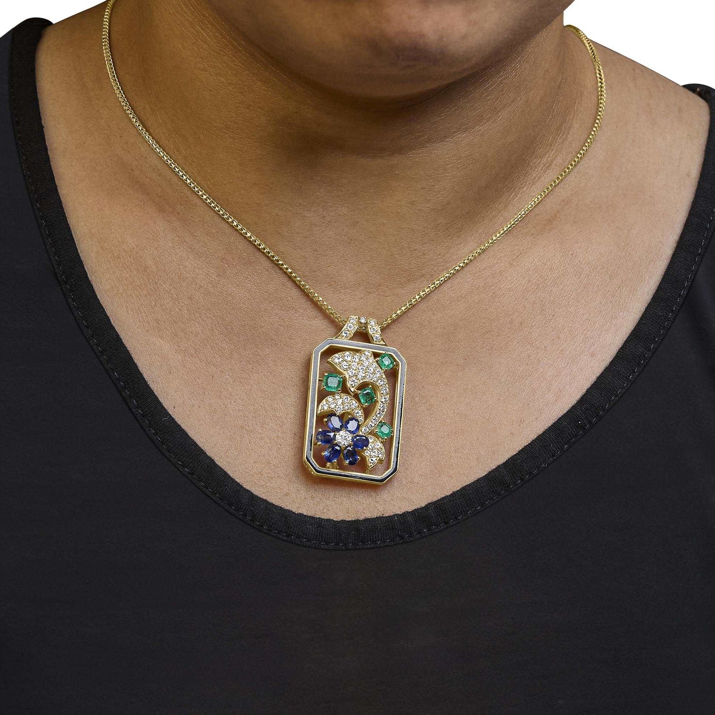 Oceanheart Sigil dolphin pendant in 18K yellow gold with diamonds, sapphires, and emeralds on a gold chain worn on a neck