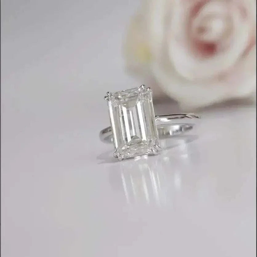 Close-up of a silver ring featuring a 5ct emerald-cut diamond Eternity Prism on reflective surface with blurred rose background