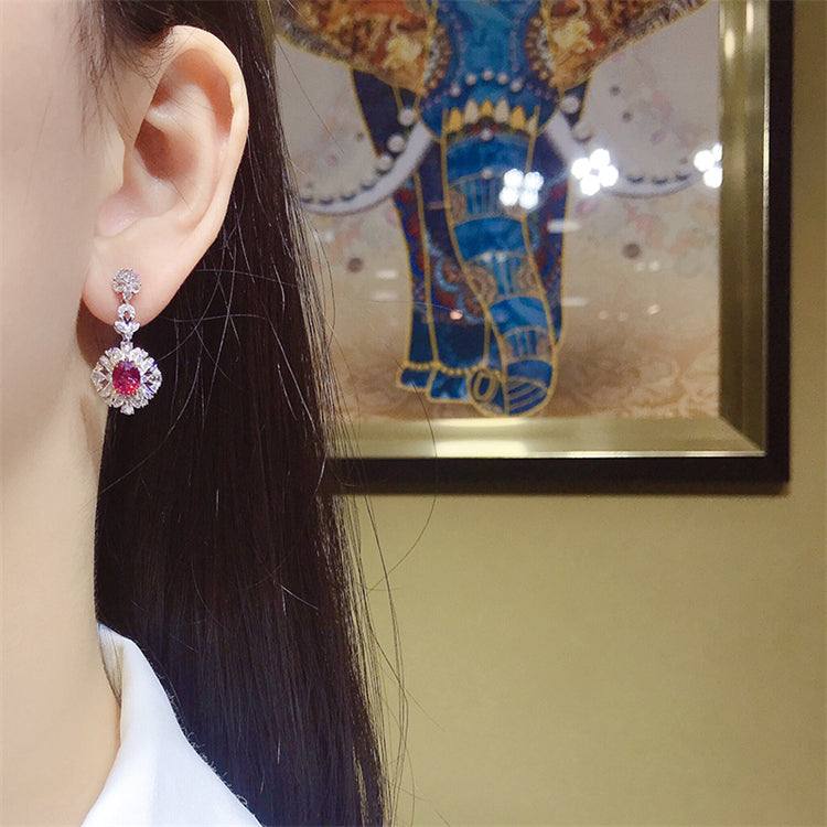 Close-up of an ear wearing The Tears of the Firebird 18k gold drop earring with a deep red ruby centerpiece surrounded by sparkling diamonds