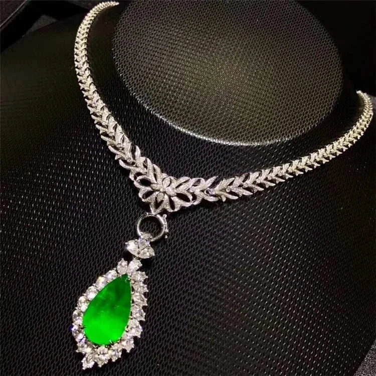 Elegant necklace featuring a pear-shaped green emerald pendant surrounded by diamonds on a silver floral chain, inspired by Heart of the Enchanted Forest design.