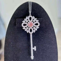 Eos’ Ember Halo pendant featuring a 0.28 ct fancy orangy-pink diamond with white diamond halo on a silver key design against black background