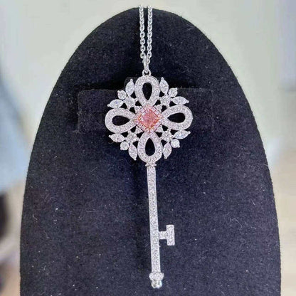 Eos’ Ember Halo pendant featuring a 0.28 ct fancy orangy-pink diamond with white diamond halo on a silver key design against black background