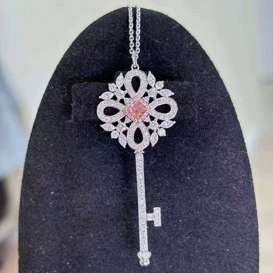 Eos’ Ember Halo pendant featuring a 0.28 ct fancy orangy-pink diamond with white diamond halo on a silver key design against black background