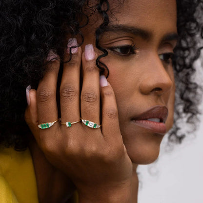 Close-up of a woman wearing 14k yellow gold Hall of Emerald Rings with natural rectangular emeralds and Asscher-cut diamonds on her fingers