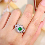 Close-up of a hand wearing the Emerald Oath of the Greenwarden ring featuring a vibrant green emerald surrounded by sparkling diamonds on an 18K gold band.