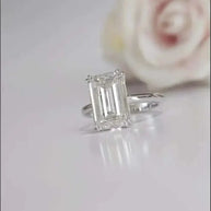 Close-up of a silver ring featuring a 5ct emerald-cut diamond Eternity Prism on reflective surface with blurred rose background