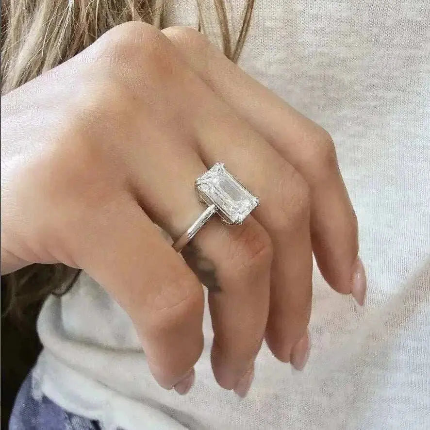 Close-up of a hand wearing the Eternity Prism 5ct emerald-cut diamond ring with a simple silver band