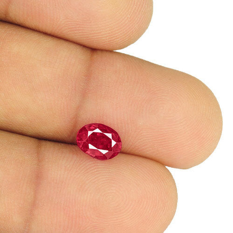 Oval 2.23-carat natural untreated ruby gem held between fingers, deep crimson red with fine clarity and intense color.